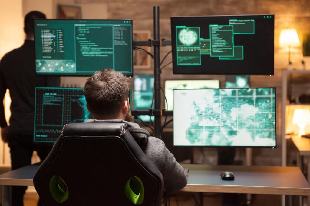 Rear view of hacker in front of computer with multiple screens