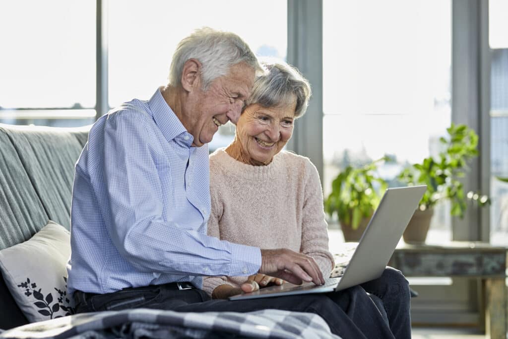 Senior couple sitting together on couch using laptop